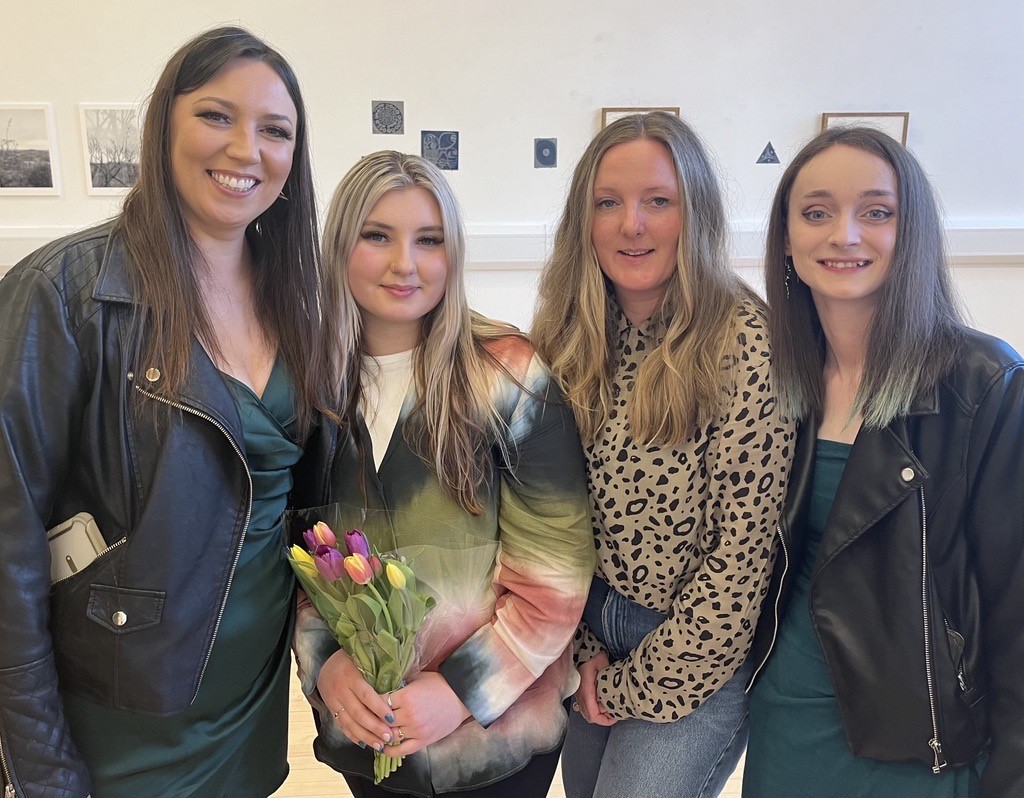 Four women standing together holding flowers in an art gallery