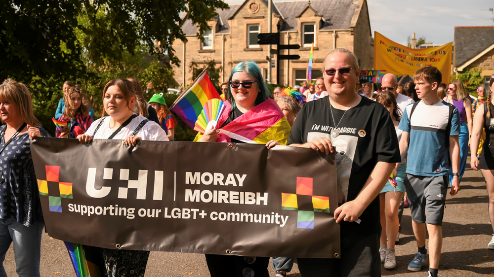 A photograph of UHI Moray staff and students at the Pride in Moray 2023 parade, they are holding a banner that says 