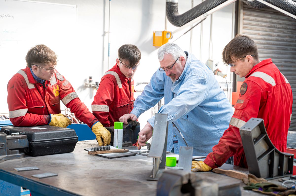 Person demonstrating manufacturing process to three students Person demonstrating manufacturing process to three students
