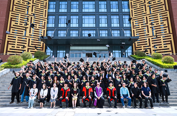 A group of students graduating wearing graduation robes outside a university building