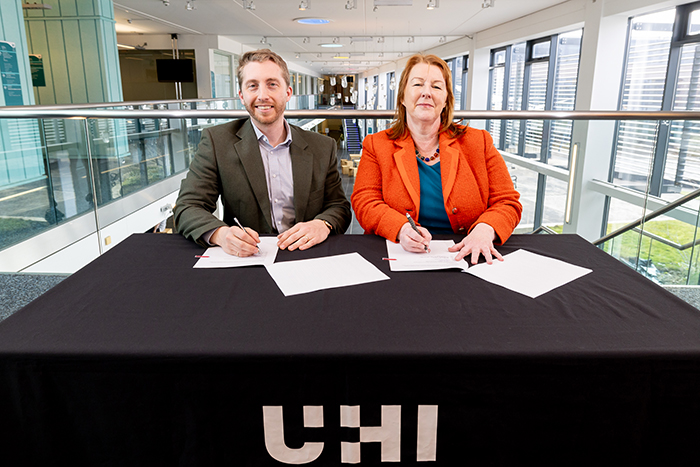 two people sitting at a table signing a document on a university campus