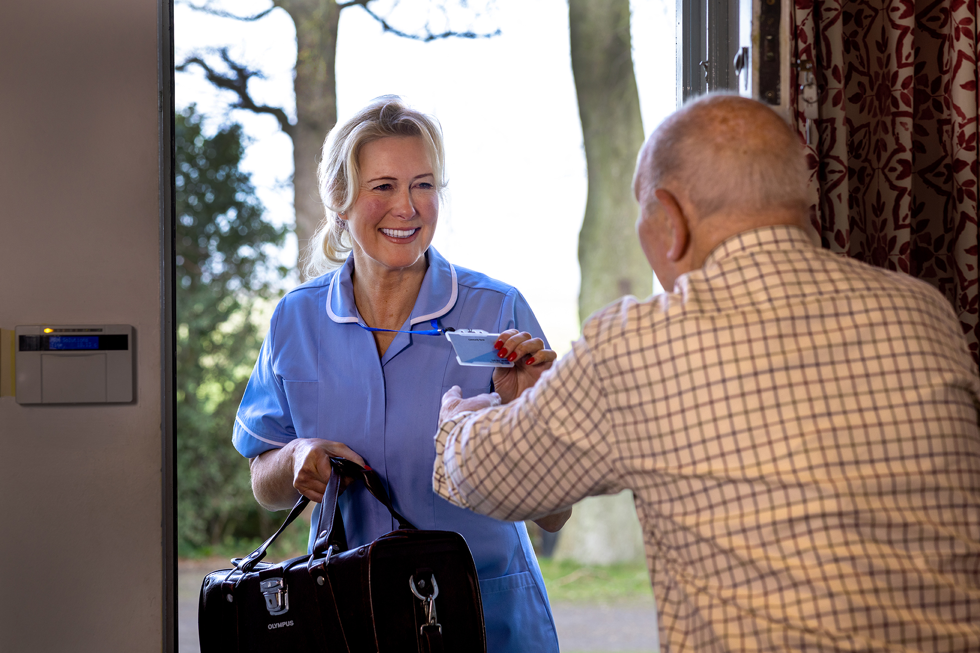 A nurse being greeted by an elderly man at a front door