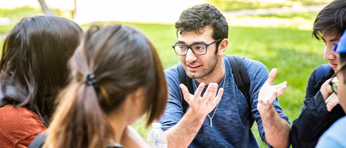 A group of students chatting on a picnic bench outside on a sunny day